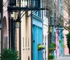 A quaint street lined with colorful houses featuring ornate ironwork balconies and flowering window boxes creates a charming urban scene