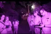 A group of people with electronic devices are standing on a dimly lit path at night captured with what appears to be night vision or infrared photography.