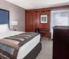 The image shows a neatly arranged hotel room with a large bed a desk with a chair a wooden wardrobe and a flat-screen TV