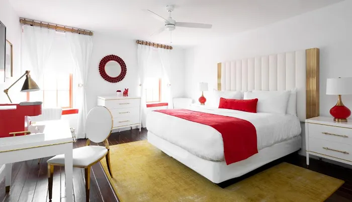 The image shows a bright and stylish bedroom with white and red decor modern furniture and pops of gold accents