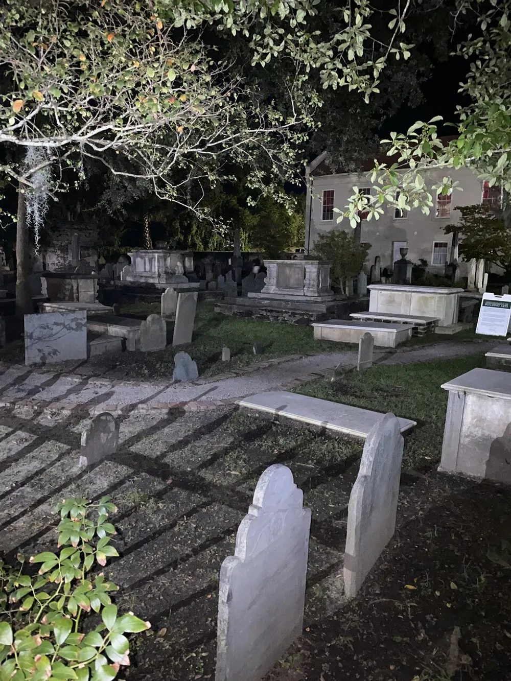 The image depicts a nighttime scene of an old spooky cemetery with various tombstones and crypts illuminated by artificial light