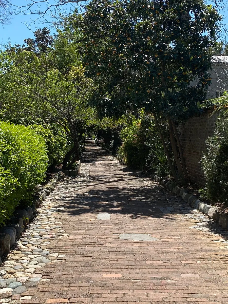 An inviting brick pathway is lined with cobblestones and flanked by lush greenery under a bright blue sky.