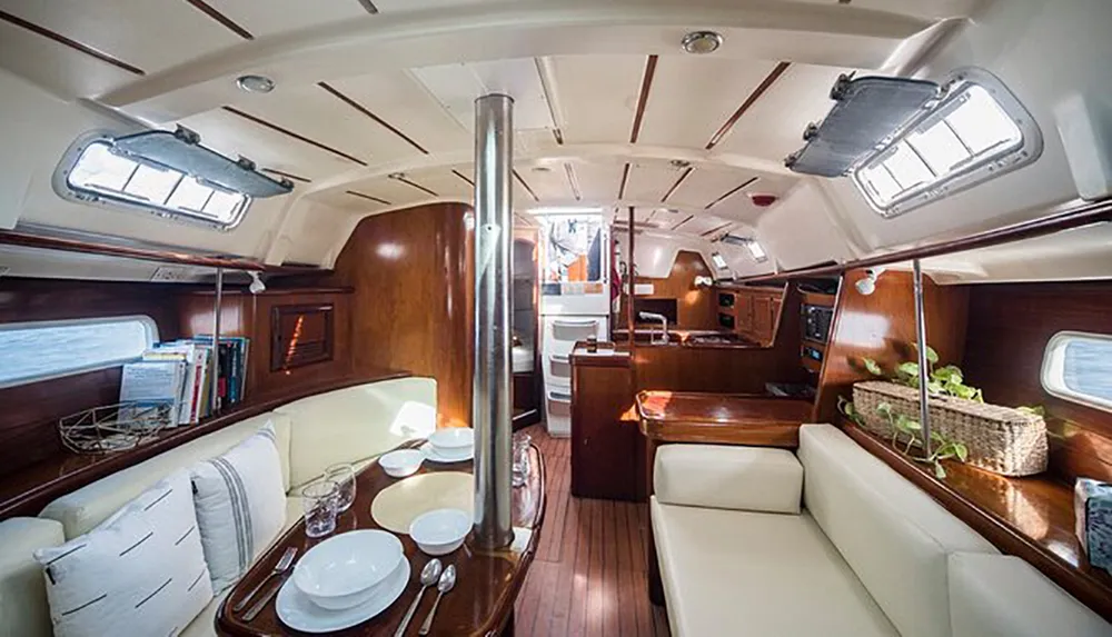 The image shows a luxurious and well-appointed sailboat cabin featuring a dining area wood paneling and ample natural light from hatches and portholes