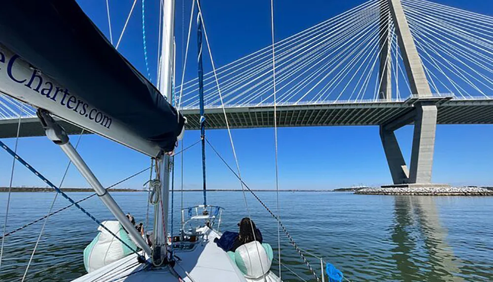 A person is enjoying a sailboat ride on a clear day with a view of a modern suspension bridge in the background