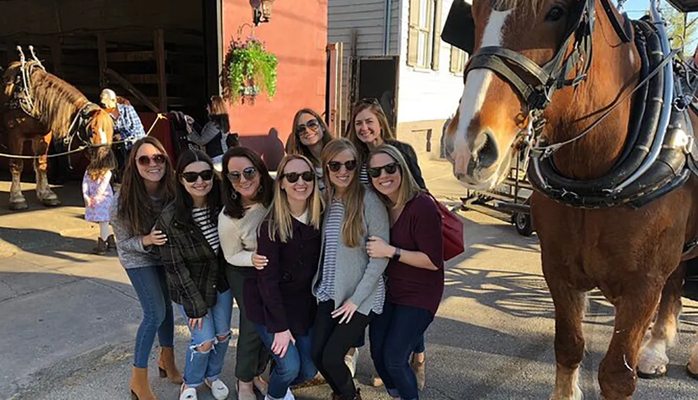 A group of cheerful people is posing for a photo in front of a large horse capturing a moment of camaraderie on a sunny day