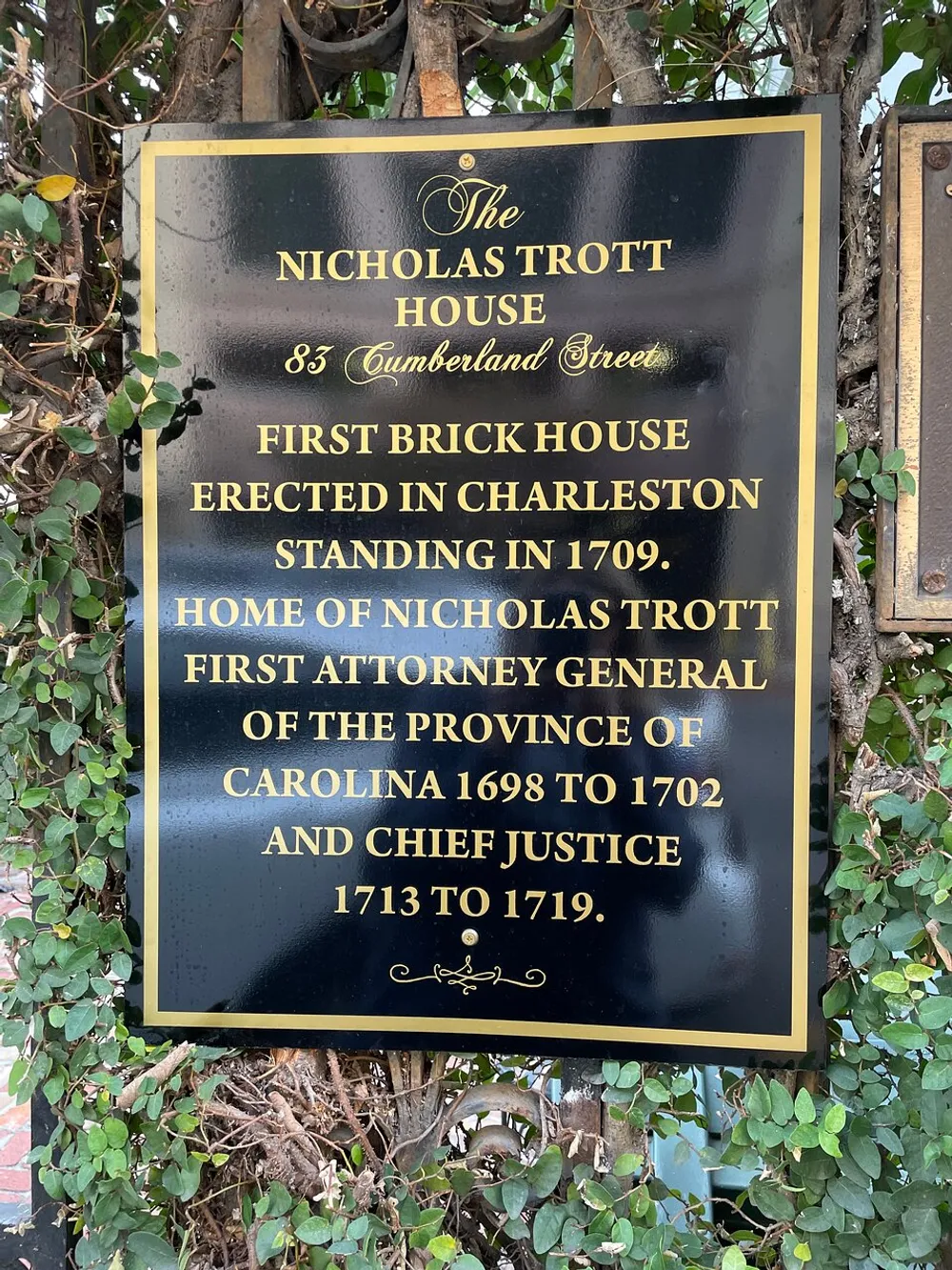 The image shows a commemorative plaque for the Nicholas Trott House in Charleston indicating it as the first brick house erected in the city in 1709 and the home of Nicholas Trott who was the Attorney General and Chief Justice of the Province of Carolina
