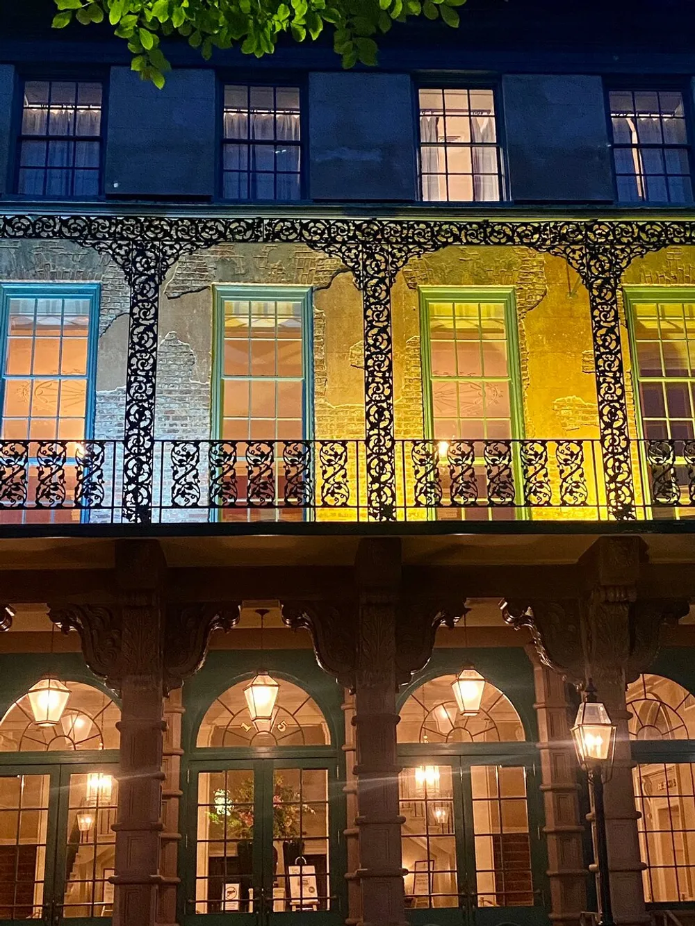The image shows the illuminated facade of a building at night characterized by its ornate iron balcony railings and contrasting window lighting