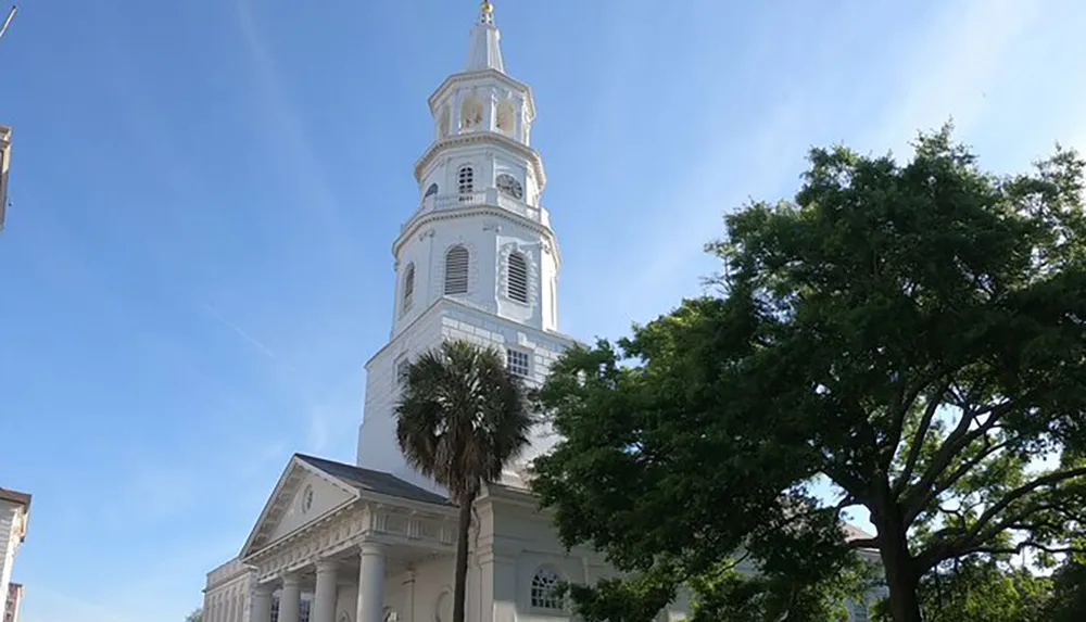 The image features a tall white church steeple rising above the surrounding trees against a clear blue sky