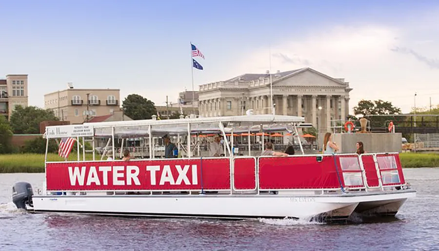 A water taxi with passengers on board is cruising near the shore with a large building in the background.