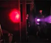 The image shows people in a dimly lit room with a red light on the left one person filming with a device emitting blue light and another observing intently