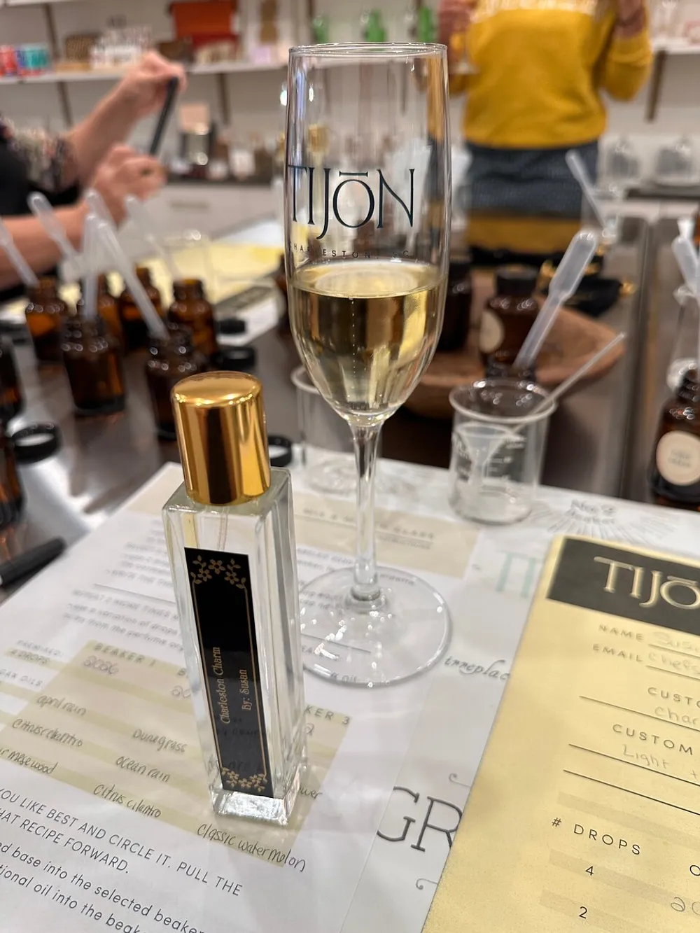 A glass of champagne and a personalized perfume bottle are on a table amidst a fragrance creation workshop or custom perfume consultation