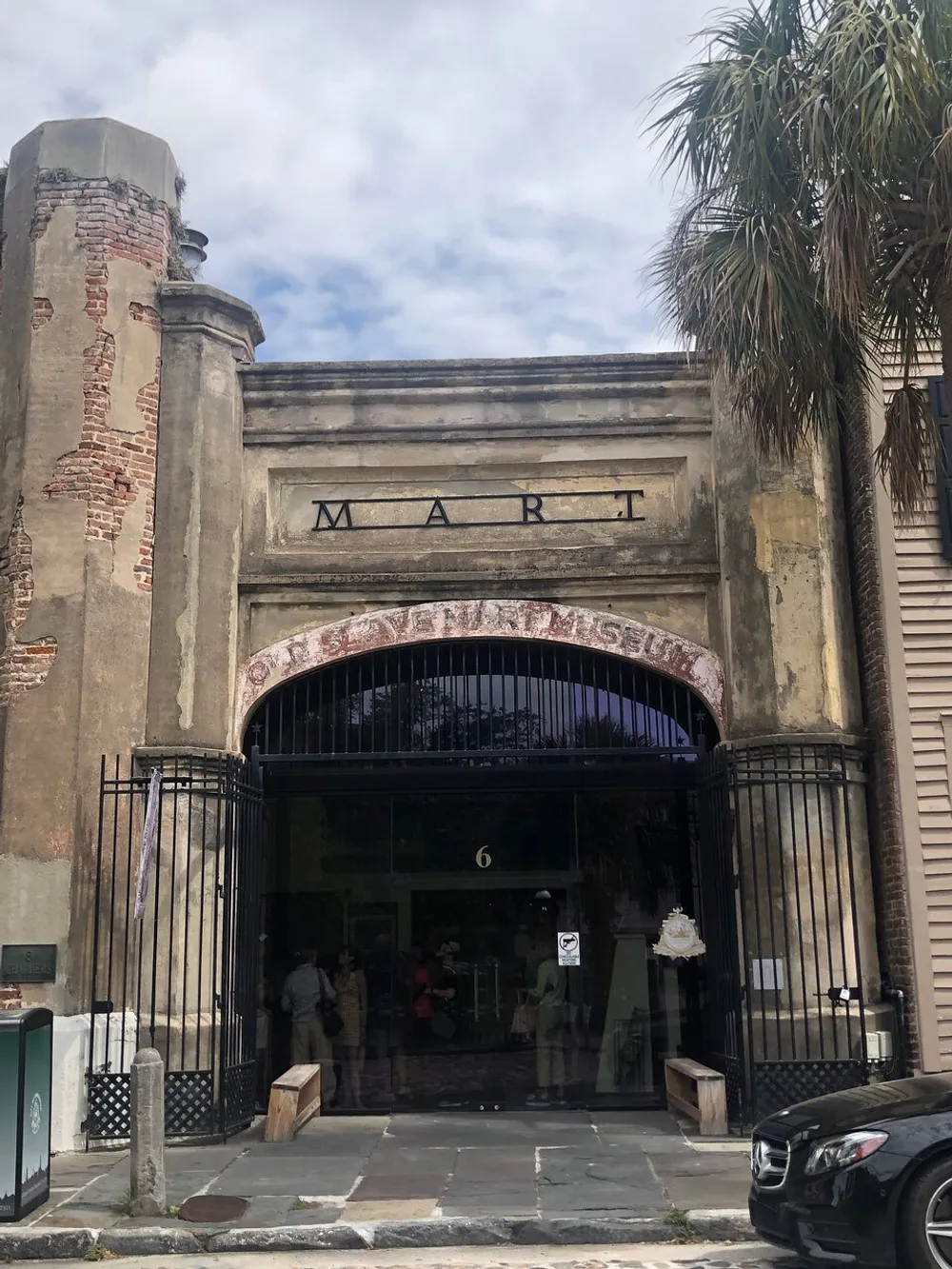 The image displays the entrance to a building with the word MART inscribed above the archway featuring a weathered facade and people near the doorway