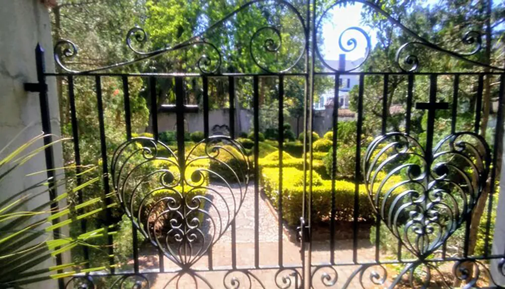 An ornate wrought iron gate opens up to a sunlit garden with bright green shrubbery