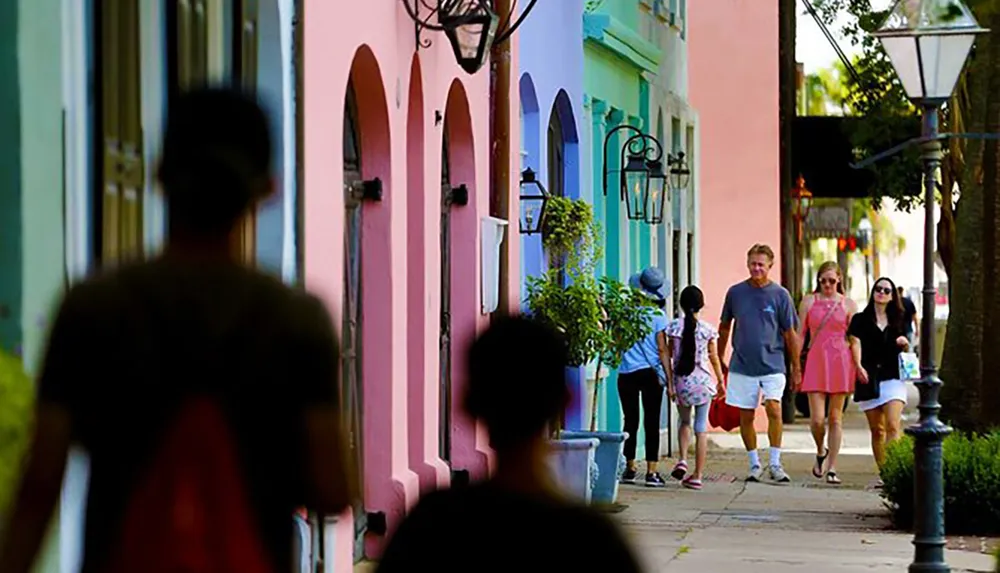 This image shows people walking by colorful buildings on a sunny tree-lined street capturing a moment of urban life