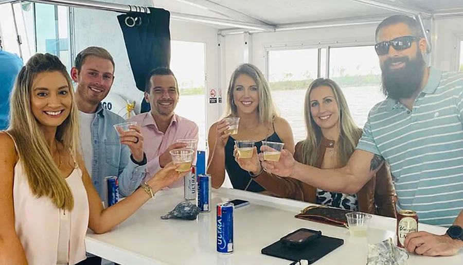 A group of six smiling adults are toasting with drinks aboard a boat.
