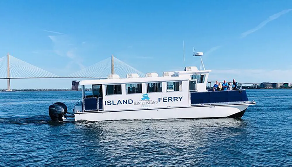 A ferry named Island Daniel Island Ferry is cruising on the water with passengers on board with a large cable-stayed bridge visible in the background