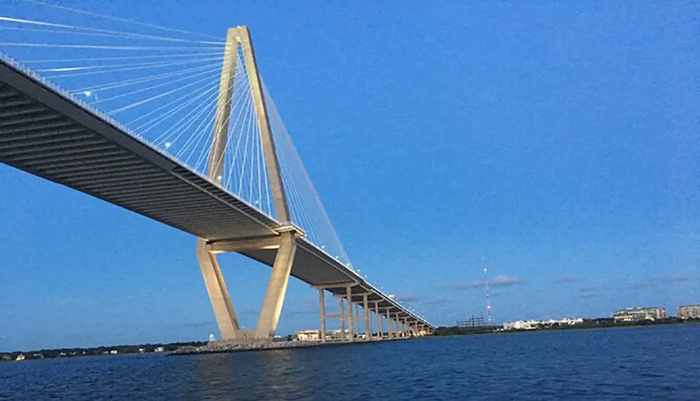 The image shows a long cable-stayed bridge extending over a body of water under a clear blue sky