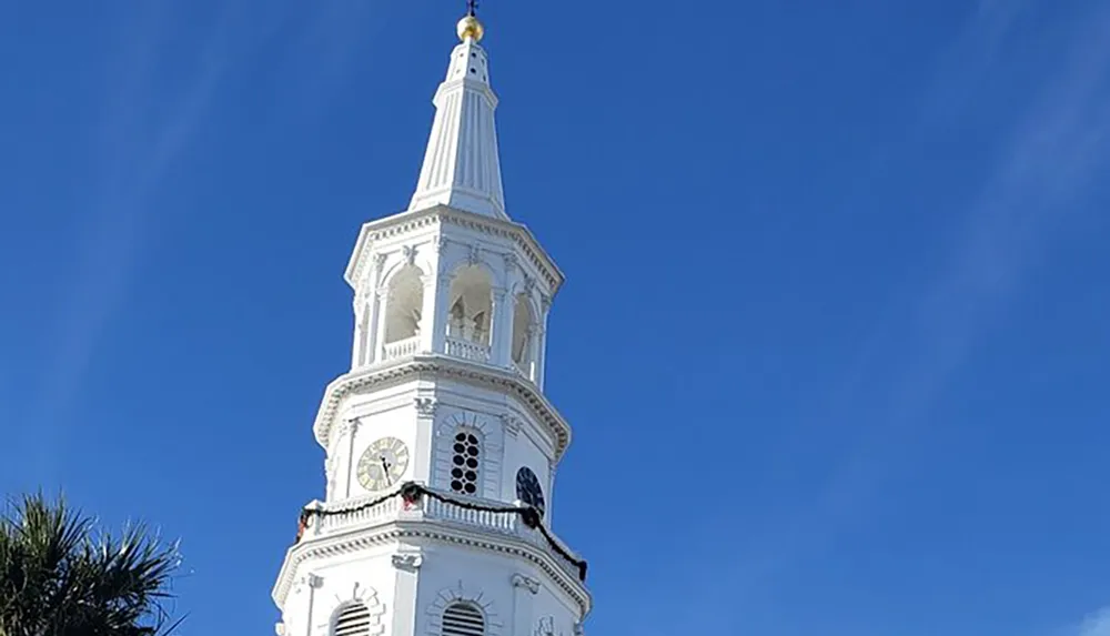 The image shows a tall white ornate steeple with clock faces against a clear blue sky