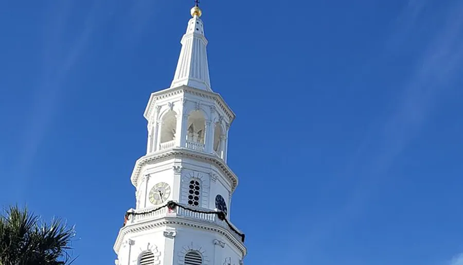 The image shows a tall, white, ornate steeple with clock faces against a clear blue sky.