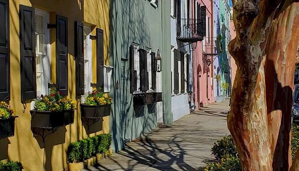 A quaint urban street lined with colorful houses and flower-filled window boxes casting long shadows in bright sunshine