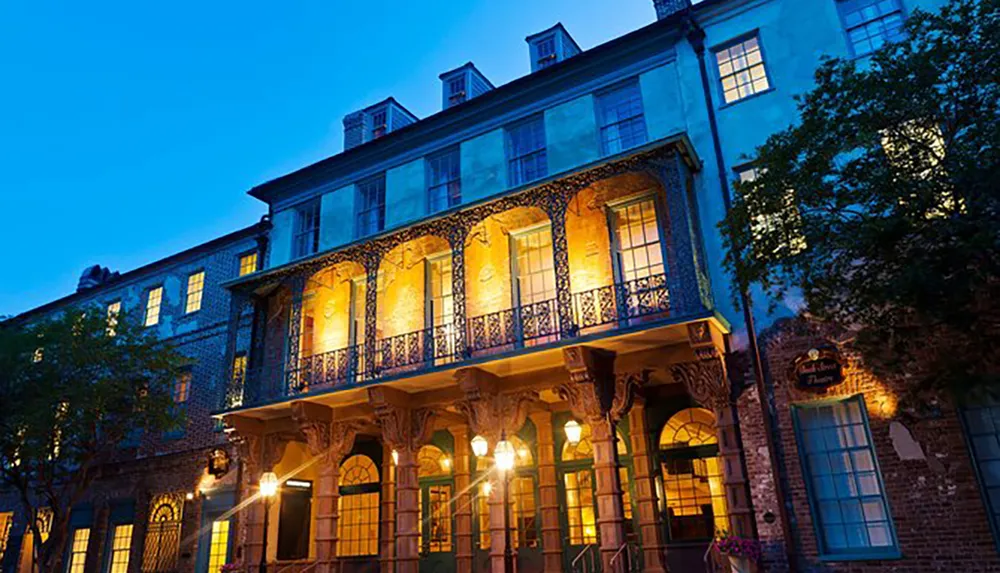 The image shows a historic building at dusk with illuminated balconies and ornate ironwork invoking a sense of old-world charm