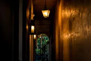 The image shows a dimly lit narrow passageway with hanging lanterns leading towards a door with intricate designs.