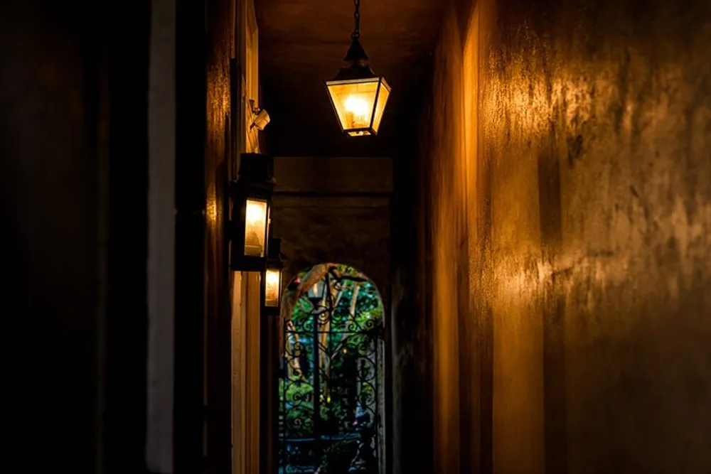 The image shows a dimly lit narrow passageway with hanging lanterns leading towards a door with intricate designs