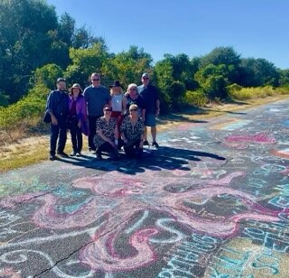 A group of people is standing on a pathway adorned with colorful chalk drawings surrounded by greenery under a clear sky