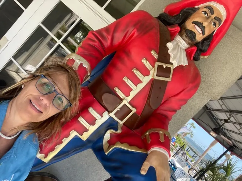 A person is smiling for a selfie with a colorful life-sized pirate statue