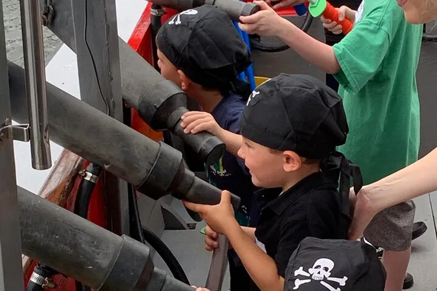 Children in pirate hats are playing with a ship's wheel and looking through a mounted spyglass.