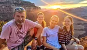 Four individuals are posing for a photo during a sunset with a scenic canyon backdrop.