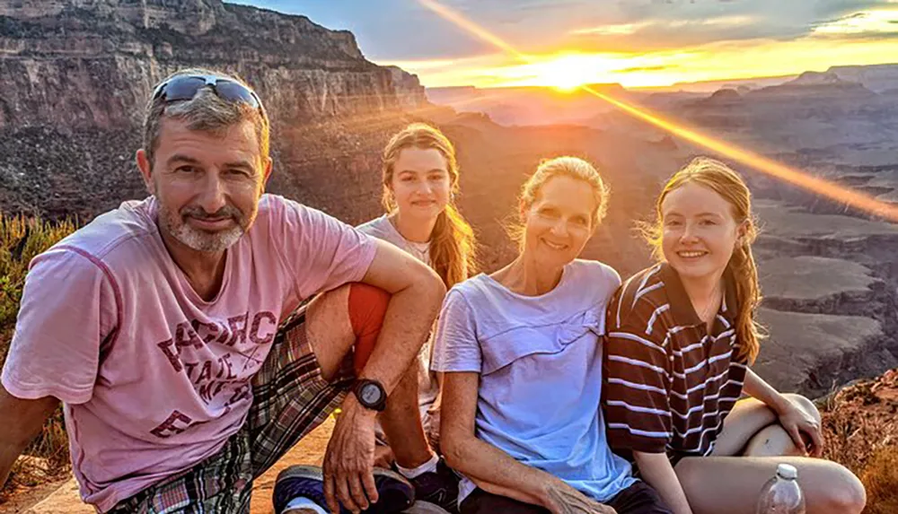 Four individuals are posing for a photo during a sunset with a scenic canyon backdrop
