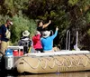 A group of people enjoy a guided tour on a large inflatable boat on a calm river surrounded by woodland