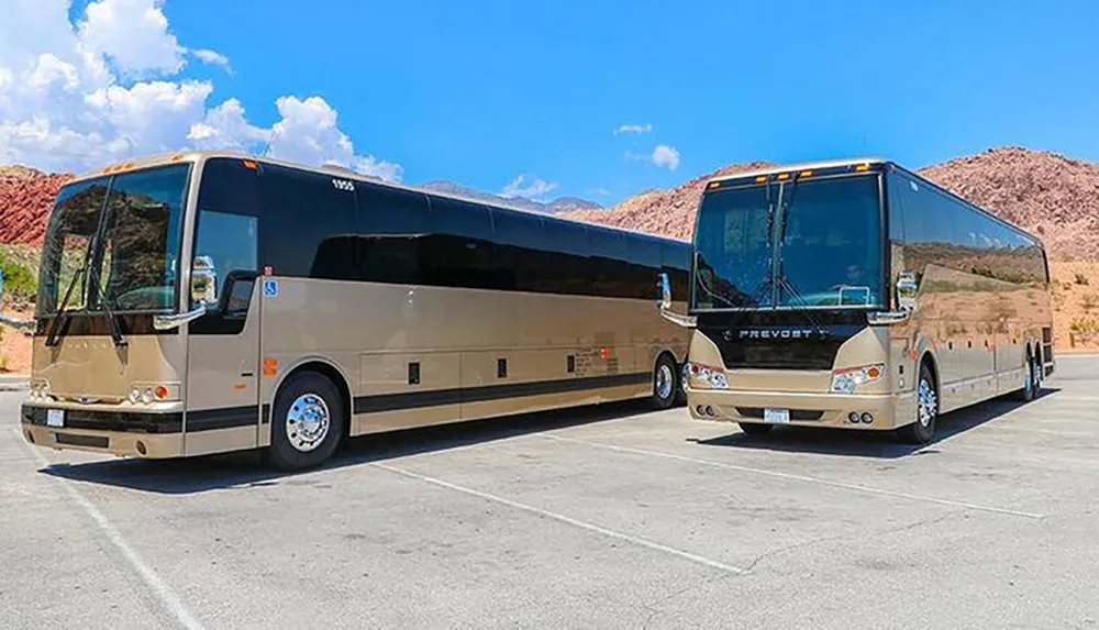 Two luxury coaches are parked side by side in an outdoor lot with a rocky landscape in the background