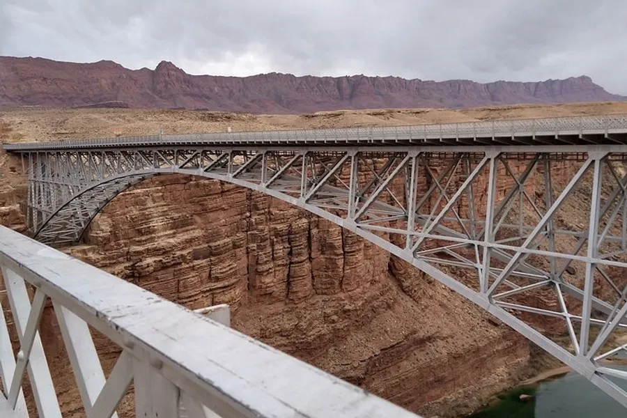 A large steel arch bridge spans a deep canyon with rugged, desert mountain scenery in the background.