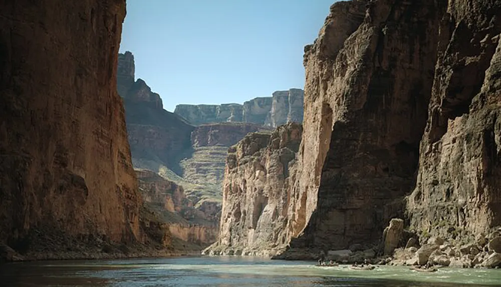 The image shows a serene river flowing through a towering canyon with steep rock cliff sides under a clear sky