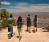 A group of tourists is engaging with a guide near the edge of a canyon with a pink Jeep Tours vehicle visible in the foreground