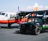 A modified off-road vehicle with Buck Wild Grand Canyon Hummer Tours branding is parked beside a Twin Otter aircraft with Grand Canyon Airlines on its tail on a clear day at an airport tarmac