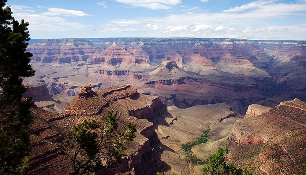This image captures a vast and colorful view of the Grand Canyon under a partly cloudy sky