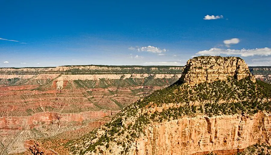 This image captures a vast, rugged landscape showcasing a prominent cliff formation under a blue sky, typical of the Grand Canyon's striking geological features.