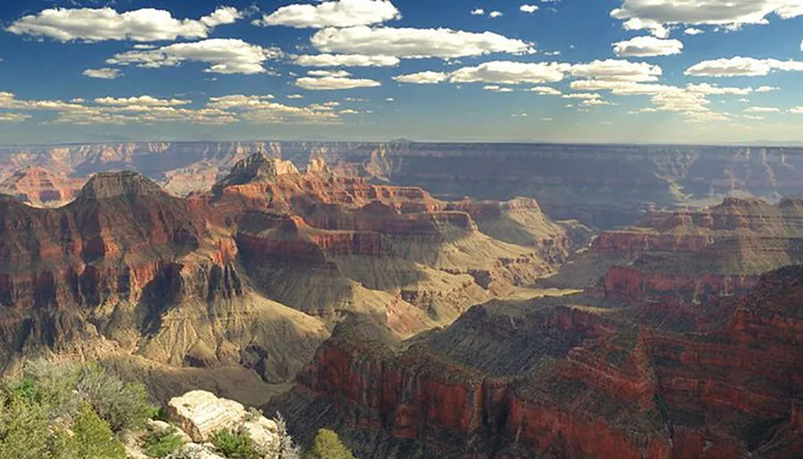 The image is a stunning view of the Grand Canyon, showcasing its layered red rock formations and vast scale under a partly cloudy sky.