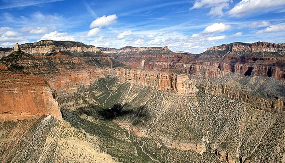 The image depicts the vast and rugged landscape of the Grand Canyon under a blue sky dotted with clouds