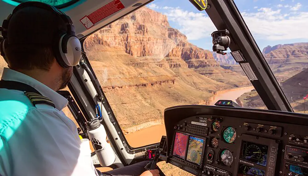 A helicopter pilot navigates the aircraft above a winding river in a canyon possibly the Grand Canyon observed from the cockpits perspective