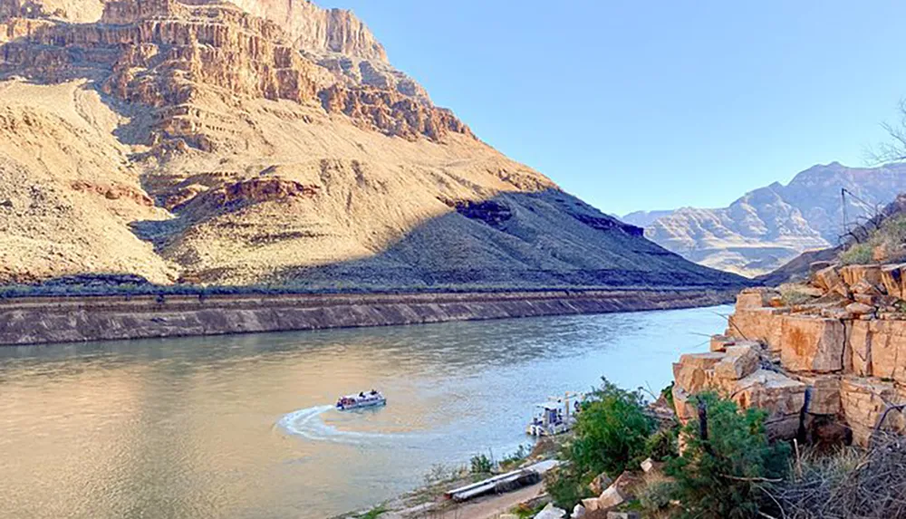 A boat navigates the tranquil waters of a river flanked by towering canyon walls under a clear sky