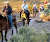 A group of people is enjoying a horseback ride along a trail in a natural bushy setting led by a person wearing a cowboy hat