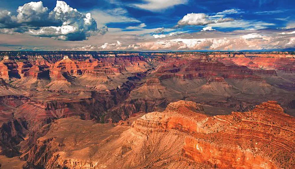 This is a panoramic view of the Grand Canyon showcasing its vast expanse and layered red rock formations under a dramatic cloudy sky