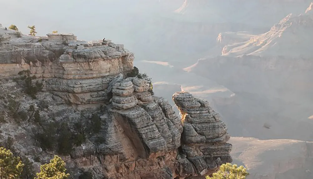A person sits contemplatively on the edge of a rugged cliff overlooking the vast and layered expanse of the Grand Canyon bathed in soft sunlight