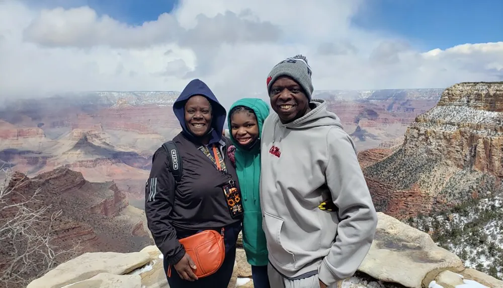 Three people are smiling for a photo in front of the snow-dusted ridges of the Grand Canyon