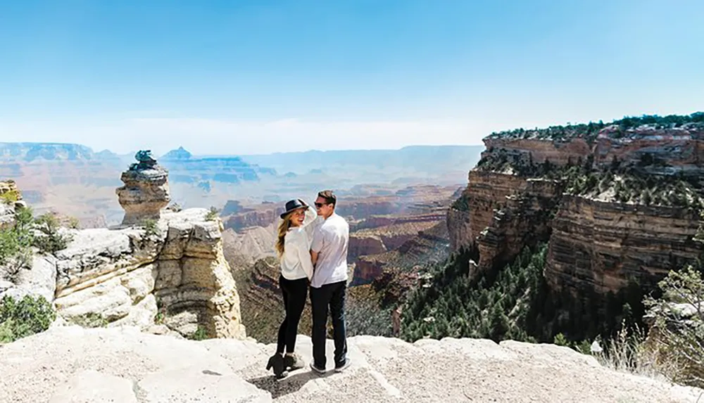 Two people are standing together overlooking the vast and scenic landscape of the Grand Canyon under a clear blue sky
