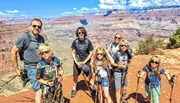 A group of six individuals, appearing to be a family, is posing with hiking sticks against the backdrop of the Grand Canyon under a clear blue sky.
